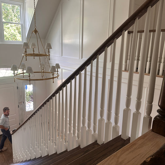 Finished custom staircase in Atlanta with white turned balusters, dark red oak handrail, and a brass chandelier in the entry