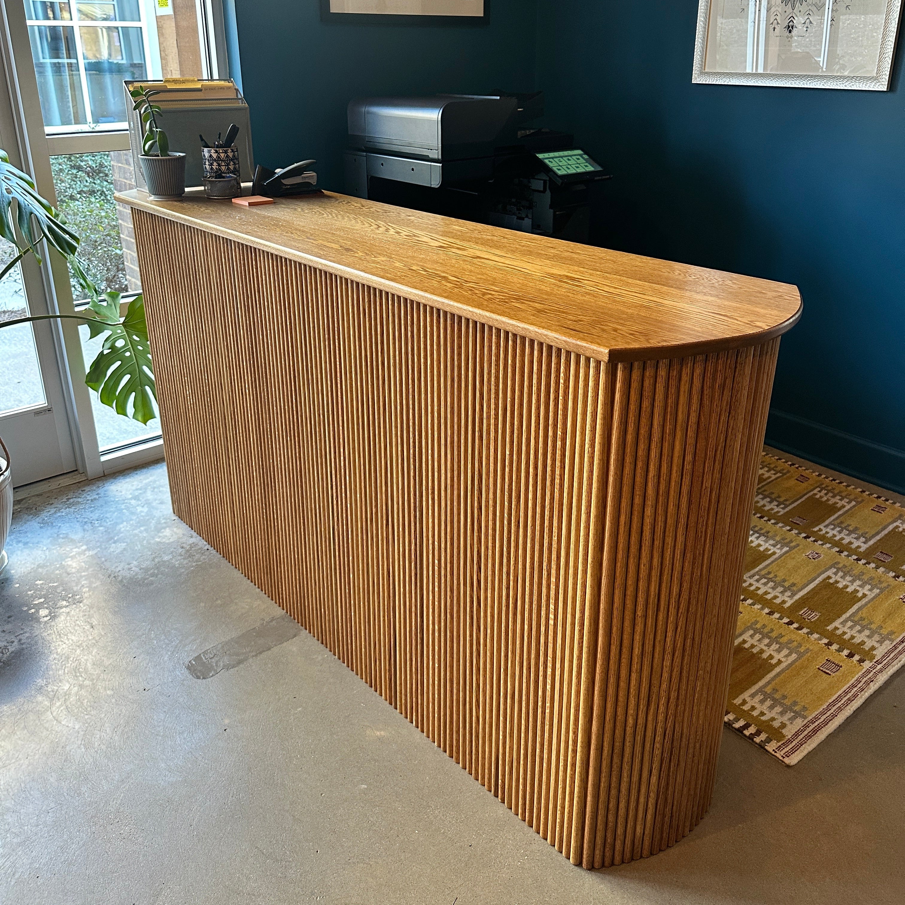 White oak tambour office desk in a room with blue walls and framed pictures.