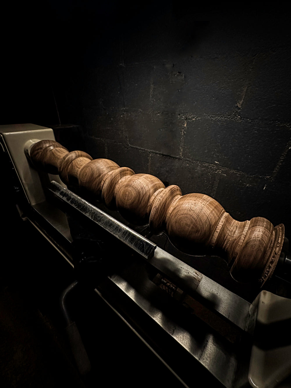 A turned walnut bed post resting on the lathe